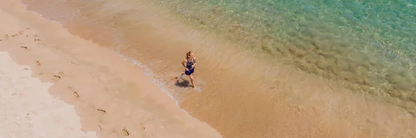 BANNER, FORMATO LARGO Corredor corriendo por la playa junto al océano - vista desde arriba. Mujer atleta entrenando ejercicio cardiovascular haciendo ejercicio matutino. Héroe plano vista avión no tripulado, un montón de espacio de copia — Foto de Stock