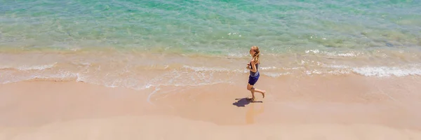 BANNER, LONG FORMAT Coureur courant sur la plage au bord de l'océan - vue d'en haut. Femme athlète entraînement cardio jogging faire de l'entraînement matinal. Vue aérienne de drone de héros, beaucoup d'espace de copie — Photo