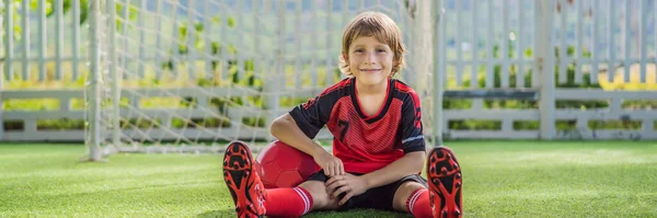 BANNER, FORMATO LUNGO Piccolo ragazzo carino in uniforme da calcio rossa che gioca a calcio, calcio sul campo, all'aperto. Bambino attivo che fa sport con i bambini o il padre, sorridente ragazzo felice divertirsi in estate — Foto Stock