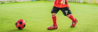 BANNER, BANNER, UZUN kırmızı futbol üniformalı küçük şirin çocuk futbol oynuyor, futbol sahada, dışarıda. Aktif çocuk çocuklarla ya da babayla spor yapıyor, gülen mutlu çocuk yazın eğleniyor.