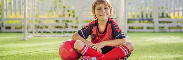 BANNER, LONG FORMAT Little cute kid boy in red football uniform playing soccer, football on field, outdoors. Active child making sports with kids or father, Smiling happy boy having fun in summer