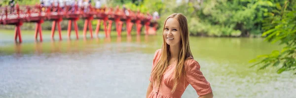 BANNER, LONG FORMAT Kaukasiska kvinna resenär på bakgrund av Red Bridge i offentlig park trädgård med träd och reflektion i mitten av Hoan Kiem Lake i centrum Hanoi. Vietnam återupptas efter — Stockfoto