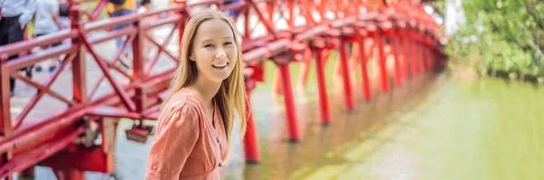 BANNER, LONG FORMAT Femme caucasienne voyageuse sur fond de pont rouge dans le jardin du parc public avec des arbres et une réflexion au milieu du lac Hoan Kiem dans le centre-ville de Hanoi. Le Vietnam rouvre après — Photo