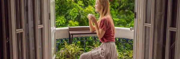 BANNER, LONG FORMAT Een roodharige vrouw staat op een balkon in erfgoedstijl te genieten van haar ochtendkoffie. Een vrouw in een hotel in Europa of Azië als toerisme herstelt van een pandemie. Toerisme — Stockfoto