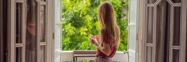 BANNER, LONG FORMAT Rudowłosa kobieta stoi na dziedzicznym balkonie i delektuje się poranną kawą. Kobieta w hotelu w Europie lub Azji, gdy turystyka wraca do zdrowia po pandemii. Turystyka ma — Zdjęcie stockowe