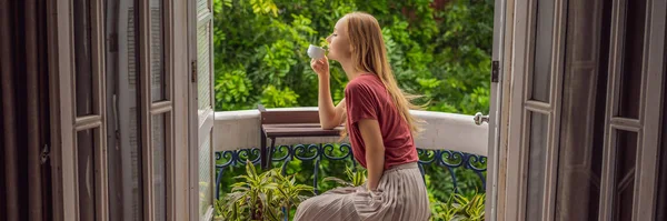 BANNER, FORMATO LUNGO Una donna dai capelli rossi si trova su un balcone in stile heritage che si gode il suo caffè mattutino. Una donna in un hotel in Europa o in Asia mentre il turismo si riprende da una pandemia. Il turismo ha — Foto Stock