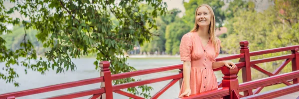 BANNER, LONG FORMAT Caucasian woman traveler on background of Red Bridge in public park garden with trees and reflection in the middle of Hoan Kiem Lake in Downtown Hanoi. Vietnam reopens after — Stock Photo, Image
