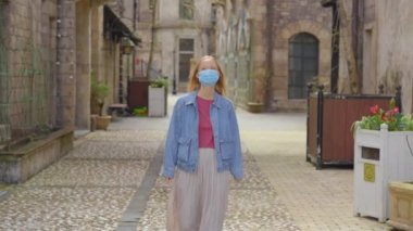 Yüz maskesi takan genç bir kadın eski Avrupa binaları arasında yürüyor. Salgın hastalıklar zamanında seyahat kavramı