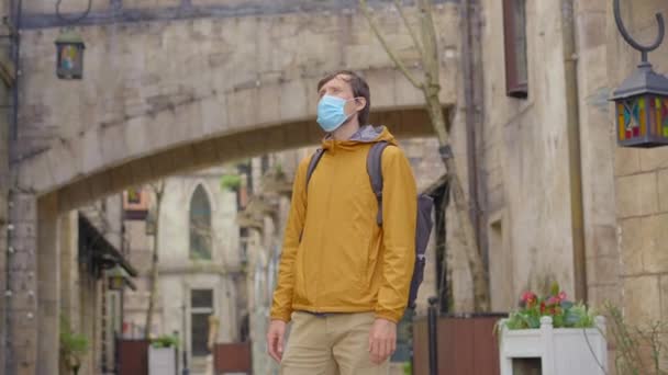 Mezi starými evropskými budovami kráčí mladý muž v masce. Koncept cestování v době pandemií — Stock video