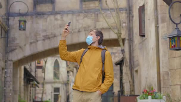 Ein junger Mann mit Gesichtsmaske geht zwischen alten europäischen Gebäuden hin und her. Konzept des Reisens in Zeiten von Pandemien — Stockvideo