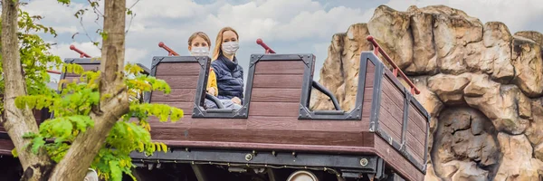 Mamá e hijo llevando una máscara médica durante el coronavirus COVID-19 en una montaña rusa BANNER, FORMATO LARGO — Foto de Stock