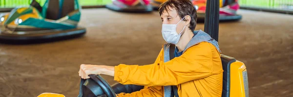 Homme portant un masque médical pendant le coronavirus COVID-19 faisant un tour dans la voiture pare-chocs au parc d'attractions BANNER, LONG FORMAT — Photo