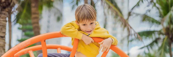 O menino sobe no playground contra o fundo das palmeiras BANNER, LONG FORMAT — Fotografia de Stock