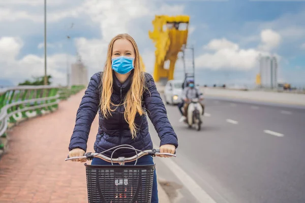 Vrouw met medisch masker tijdens COVID-19 coronavirus fietst op de drakenbrug in Da Nang — Stockfoto