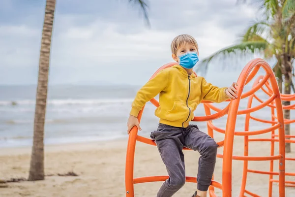 COVID-19 코로나 바이러스 (coronavirus) 에서 의료용 마스크를 착용하고 있는 소년은 야자수를 배경으로 운동장에 올라간다. — 스톡 사진