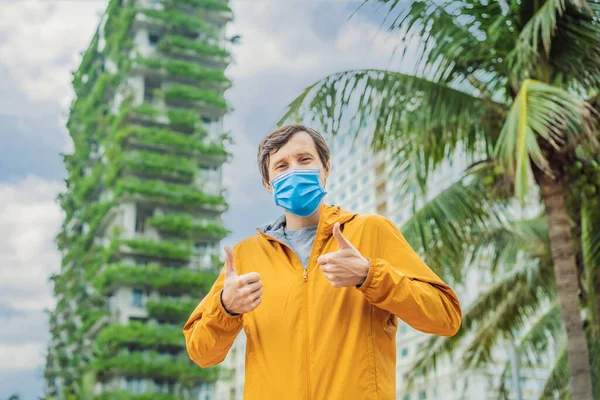 Man wearing a medical mask during COVID-19 coronavirus looks at Eco architecture. Green cafe with hydroponic plants on the facade. Ecology and green living in city, urban environment concept. Modern — Stock Photo, Image