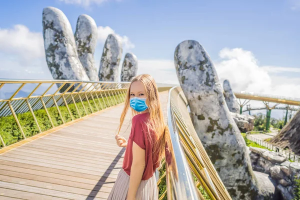 Young woman tourist wearing a medical mask during COVID-19 coronavirus at Famous tourist attraction - Golden bridge at the top of the Ba Na Hills, Vietnam — Stock Photo, Image