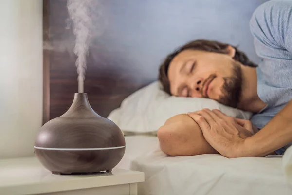 Aromatherapy Concept. Wooden Electric Ultrasonic Essential Oil Aroma Diffuser and Humidifier. Ultrasonic aroma diffuser for home. Man resting at home — Stock Photo, Image