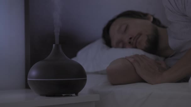 Вночі людина ковзає в ліжку з дифузором ароматерапії, який працює на підставці. Концепція глибокого та спокійного сну — стокове відео