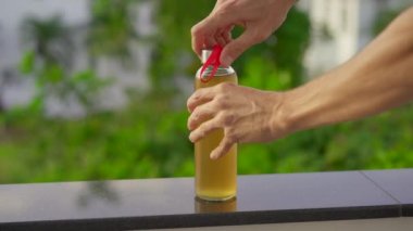 Kombucha içkisinin cam şişesini yakından çek. Adam şişeyi soğuk bir içecekle açar ve tekrar kullanılabilir metal bir pipet koyar.