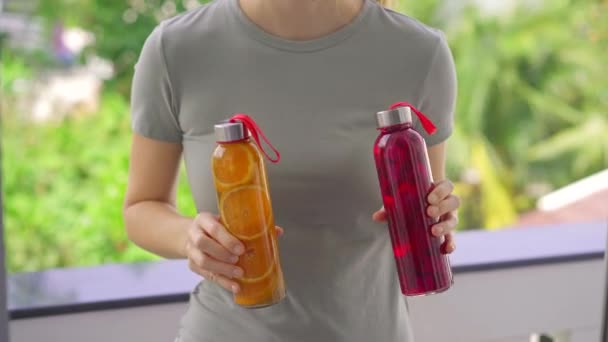 Una mujer sostiene dos botellas con bebida de kombucha en sus manos, que tienen diferentes sabores: naranja y fruta de dragón. Concepto de bebidas saludables — Vídeos de Stock