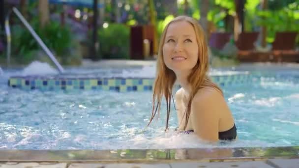 Młoda kobieta relaksuje się i świetnie się bawi w gorących źródłach kurortu z basenami z ciepłą wodą. Jest w basenie do masażu. — Wideo stockowe