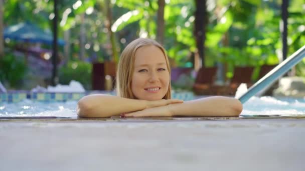Una mujer joven se relaja y se lo pasa en grande en un balneario termal con piscinas de agua caliente. Ella está en la piscina de masaje — Vídeos de Stock