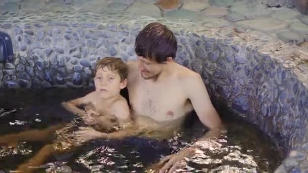 El joven y su hijo se relajan en un baño de piedra lleno de infusiones de hierbas curativas. Concepto de medicina herbal — Vídeos de Stock