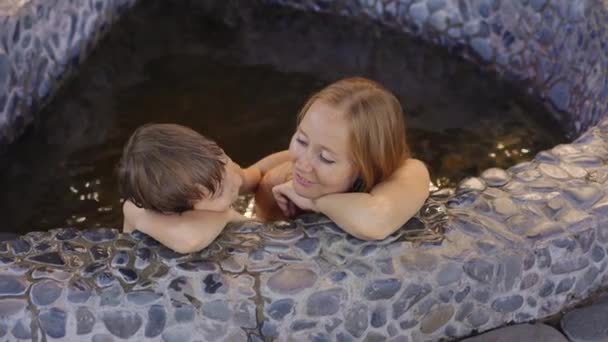 La joven y su hijo se relajan en un baño de piedra lleno de infusiones de hierbas curativas. Concepto de medicina herbal — Vídeos de Stock