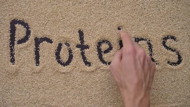 En man skriver text på svart bakgrund med quinoafrön. Han skriver text PROTEINS — Stockvideo