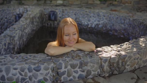 Tiro em câmara lenta. Mulher jovem relaxa em um banho de pedra cheio de infusões de ervas curativas. Conceito de fitoterapia — Vídeo de Stock