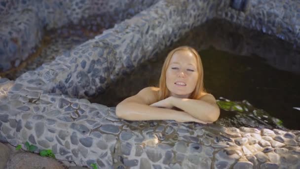 Disparo en cámara lenta. Mujer joven se relaja en un baño de piedra lleno de infusiones de hierbas curativas. Concepto de medicina herbal — Vídeos de Stock
