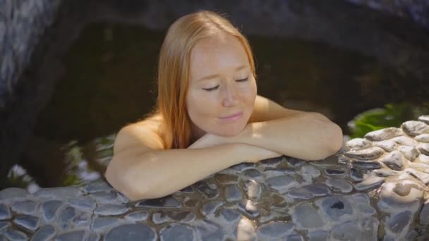 Disparo en cámara lenta. Mujer joven se relaja en un baño de piedra lleno de infusiones de hierbas curativas. Concepto de medicina herbal — Vídeos de Stock