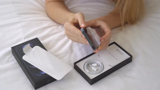 12.01.2021 - New York, USA: Ung kvinna i sovrummet öppnar sin nya Iphone 12pro — Stockvideo