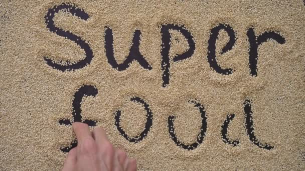 En mann skriver tekst på svart bakgrunn med quinoa-frø. Han skriver tekst SUPER FOOD – stockvideo