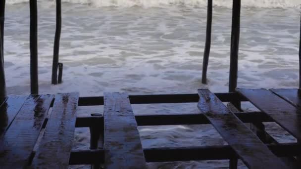 Big stormy waves and wind. View from a beach cafe on a stormy sea on a sunny day. Part of the floor was broken. Waves are coming under the floor — Stockvideo