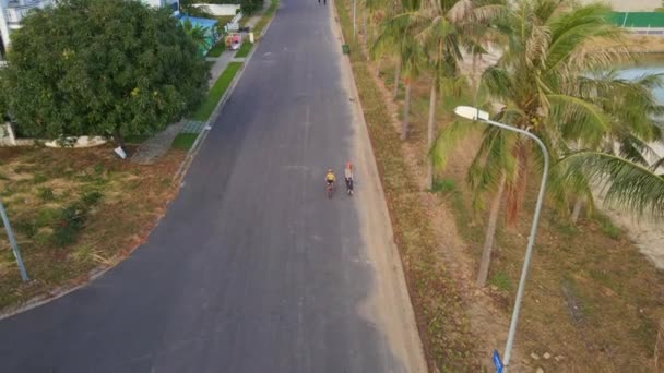 Zeitlupenaufnahme aus der Luft. Frau und Sohn fahren Tretroller und Fahrrad am Meer unter Palmen bei Sonnenuntergang — Stockvideo
