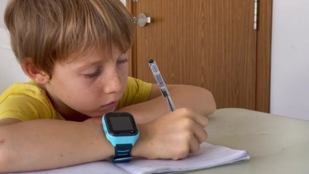 A little boy writes in a notebook. He is wearing smart watches. Children security concept — Vídeo de Stock