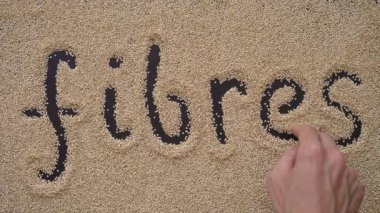 Bir adam kinoa tohumu kullanarak siyah bir arkaplan üzerine metin yazıyor. FIBRES metni yazıyor