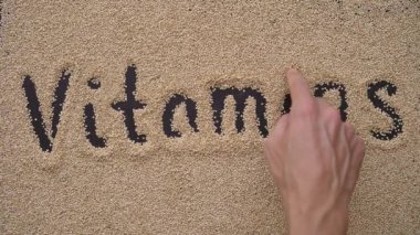Bir adam kinoa tohumu kullanarak siyah bir arkaplan üzerine metin yazıyor. VITAMINS metin yazıyor.