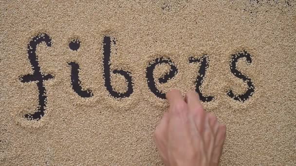 Een man schrijft tekst op een zwarte achtergrond met behulp van quinoa zaden. Hij schrijft tekst FIBERS — Stockvideo