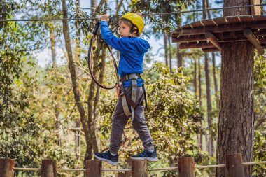 Kasklı mutlu bir çocuk, sağlıklı bir okul çocuğu yaz günü tırmanma parkında eğleniyor.