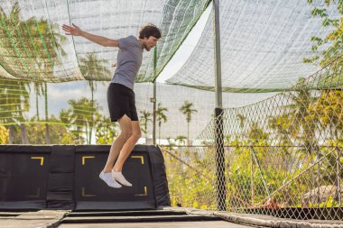 Mutlu adam trambolinde zıplıyor, palmiye ağaçlarının arka planında