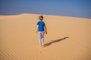 Çölde seyahat eden genç bir çocuk. Güneşli yaz gününde kumullar ve mavi gökyüzü. Seyahat, macera, özgürlük konsepti. COVID 19 karantinasından sonra turizm yeniden açıldı