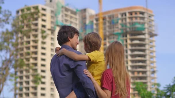 Un padre, una madre e un figlio di famiglia guardano un edificio alto che è in costruzione. Stanno discutendo dove dovrebbero comprare un appartamento — Video Stock