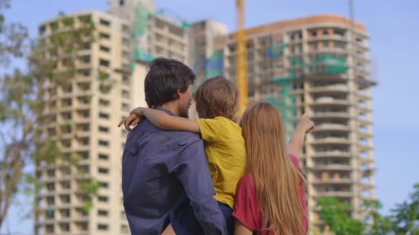 Egy családapa, anya és fia megnéznek egy magas épületet, ami építés alatt áll. Azt beszélik meg, hol vegyenek lakást. — Stock videók