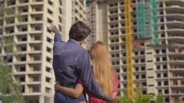 Genç bir aile inşaat halinde olan yüksek bir binaya bakıyor. Nereden daire almaları gerektiğini tartışıyorlar.