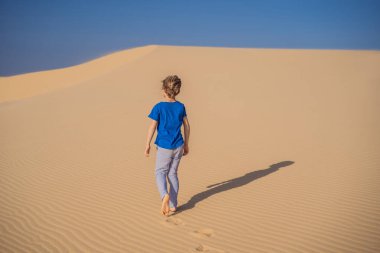 Çölde seyahat eden genç bir çocuk. Güneşli yaz gününde kumullar ve mavi gökyüzü. Seyahat, macera, özgürlük konsepti. COVID 19 karantinasından sonra turizm yeniden açıldı