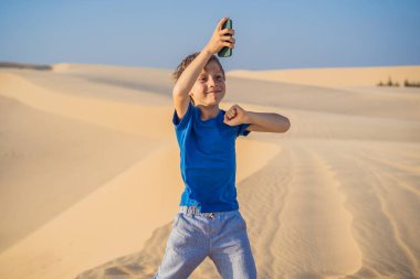 Çölde elinde akıllı bir telefonla dans eden sevimli, komik çocuk.