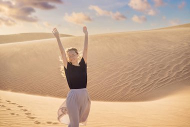 Çölde seyahat eden genç ve güzel bir kadın. Güneşli yaz gününde kumullar ve mavi gökyüzü. Seyahat, macera, özgürlük konsepti. COVID 19 karantinasından sonra turizm yeniden açıldı